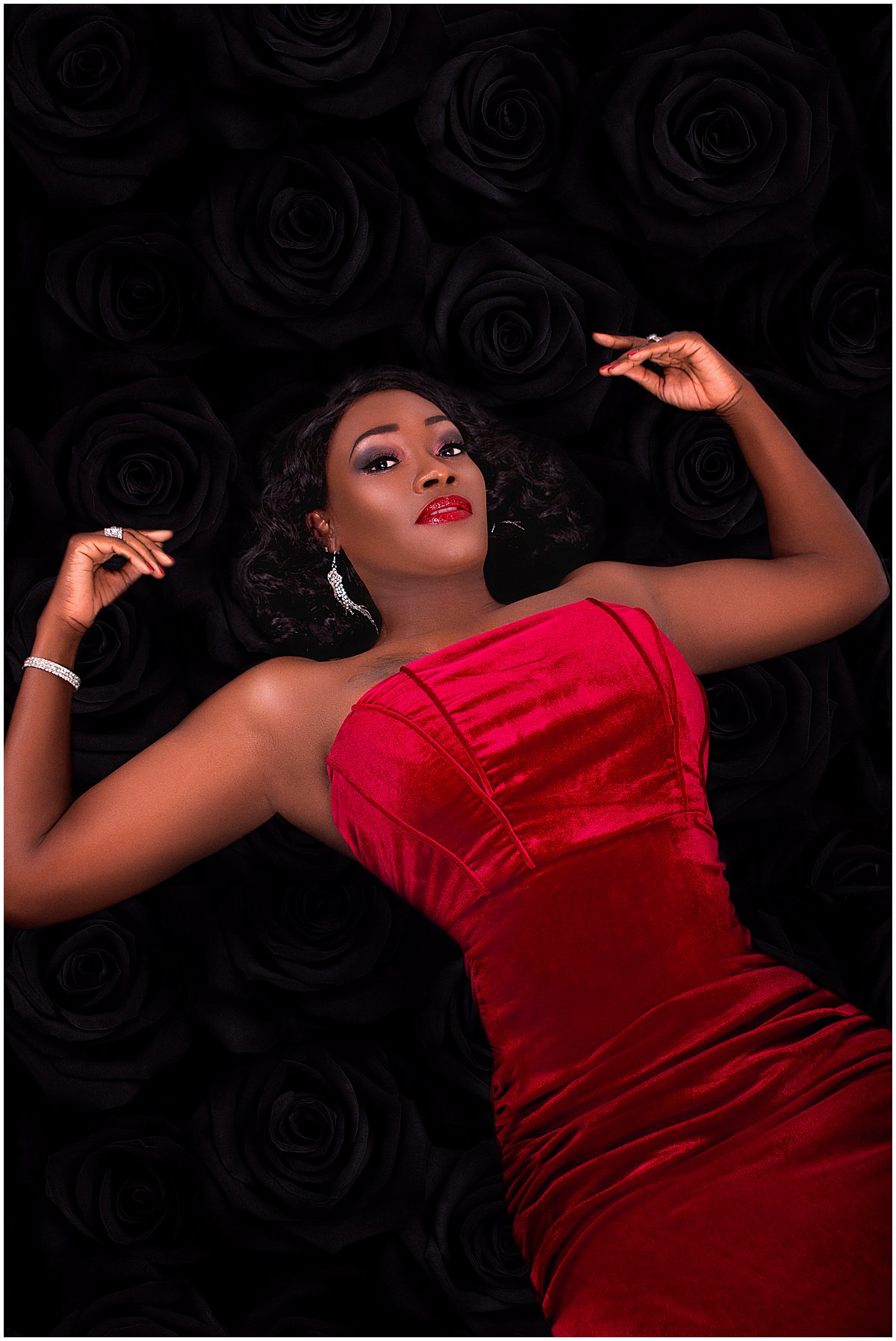 A black woman in a red gown lays on black fabric for her birthday photo session