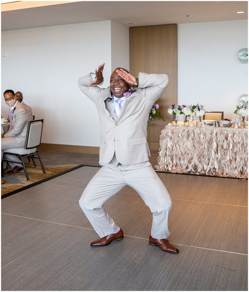 Black man in tan suit does his fraternity dance during his entrance into the reception hall, InterContinental at the Wharf in Washington, DC.