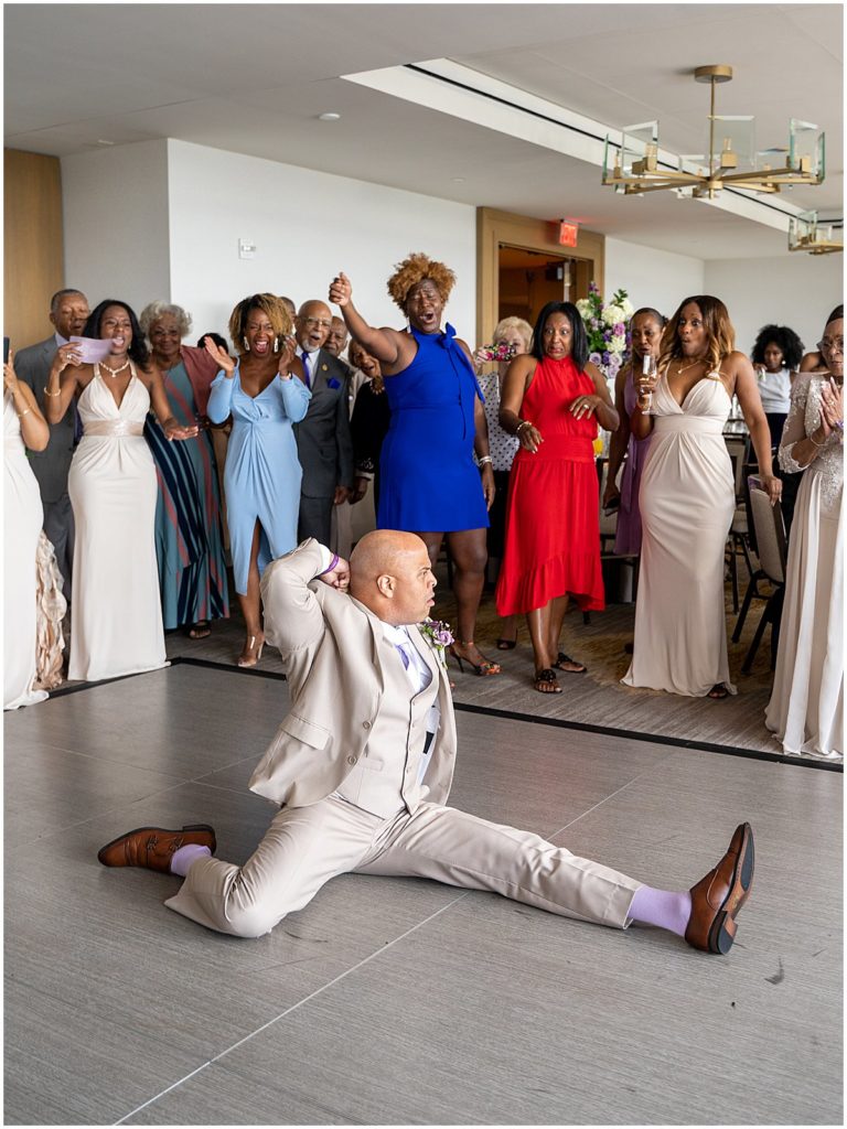 Gentleman in suit does the splits in front of a cheering crowd. Captured by Class & Style Productions, hybrid wedding photography team.