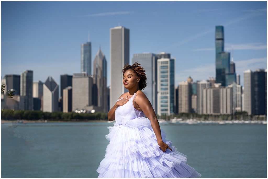 Black woman dressed in a purple gown poses with the Chicago skyline behind her.