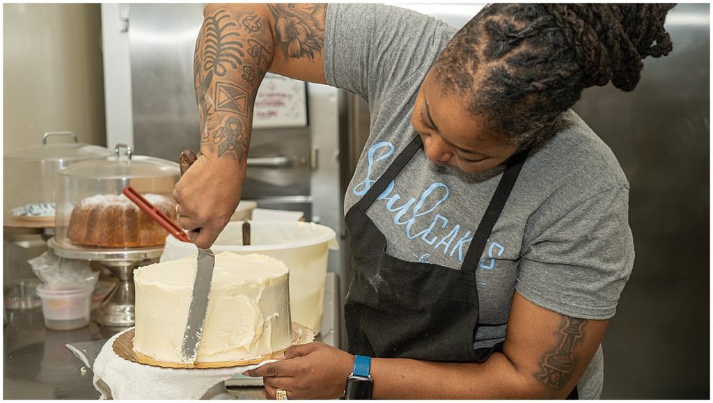 Black woman baker puts buttercream on a cake.
