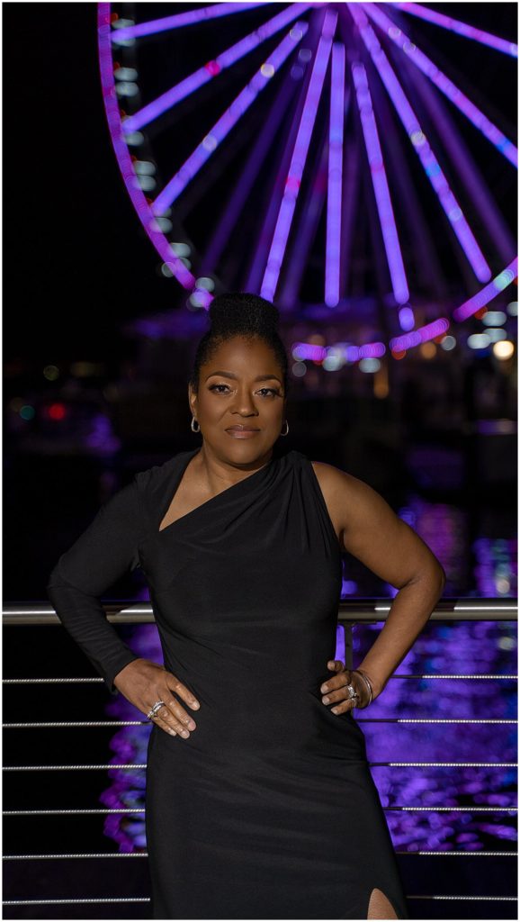 woman in black dress poses in front of ferris wheel at National Harbor