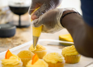 African American man decorates cupcakes with yellow frosting for an event.